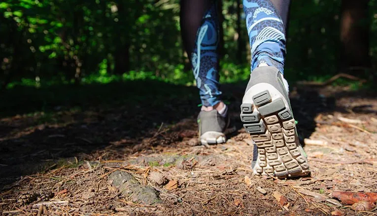 A person is walking in a forest, showcasing the soles of their shoes.